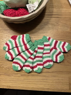 Hand-knitted striped socks in red, green, and white laid out on a wooden table with yarn basket