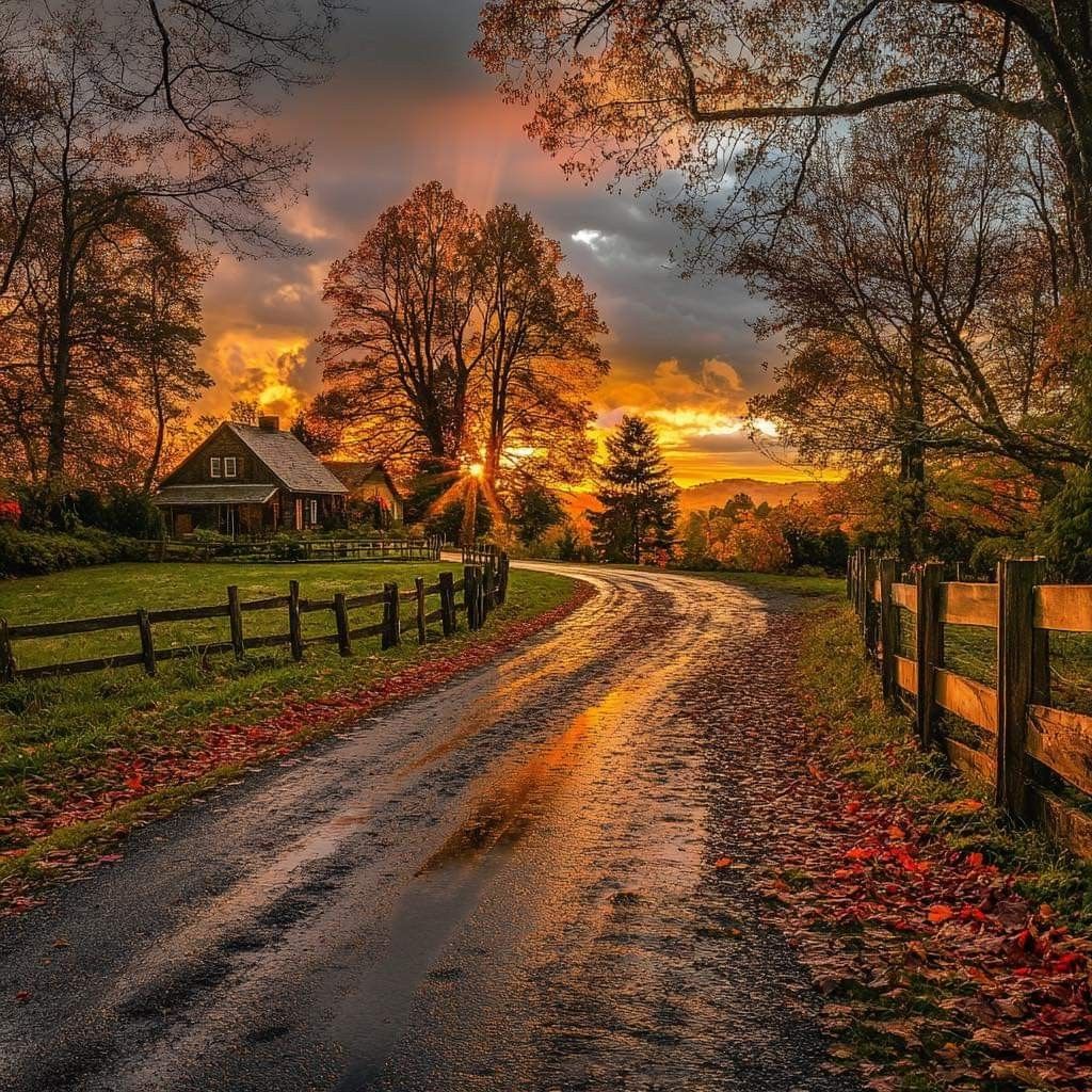 Curved country road with autumn leaves, wooden fence, trees, and vibrant sunset sky with barn in background
