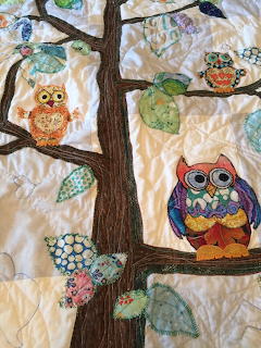 Handmade quilt with colorful appliqué owls sitting on tree branches with decorative leaves