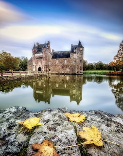 Stone castle reflected in a calm pond with autumn leaves on a foreground rock
