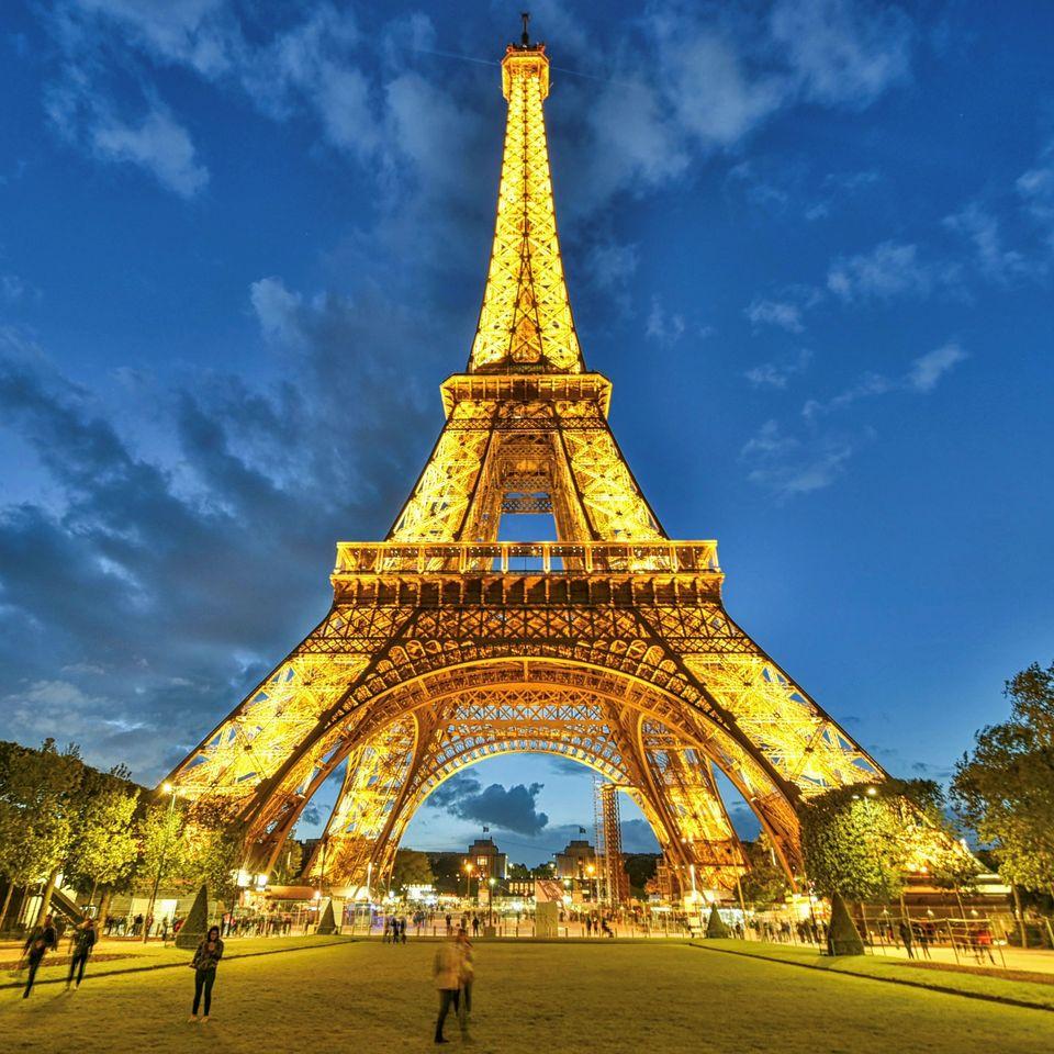 Eiffel Tower lit up at dusk with golden lights against blue sky in Paris