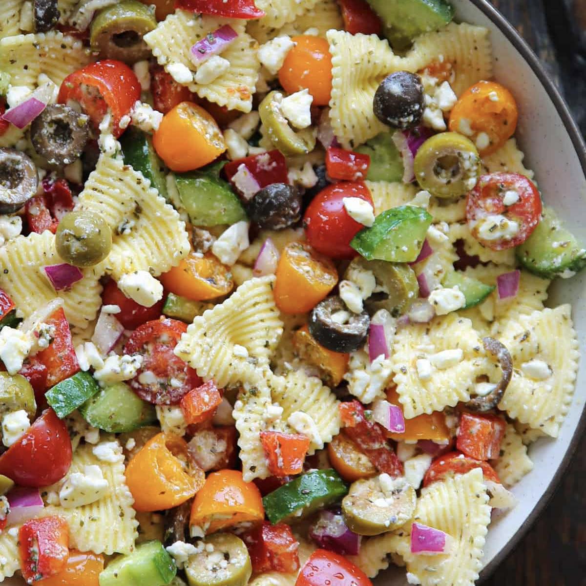 Bowl of pasta salad with bow-tie pasta, tomatoes, cucumber, olives, feta, and red onion