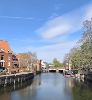 Stone bridge over the River Wensum in Norwich with brick buildings and trees along the banks