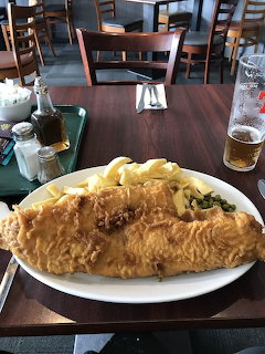 Large battered fish and chips on a white plate at a restaurant table