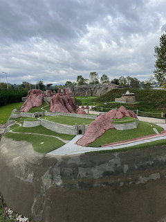 Miniature model of Belogradchik Fortress with red rock formations and green grass under cloudy sky
