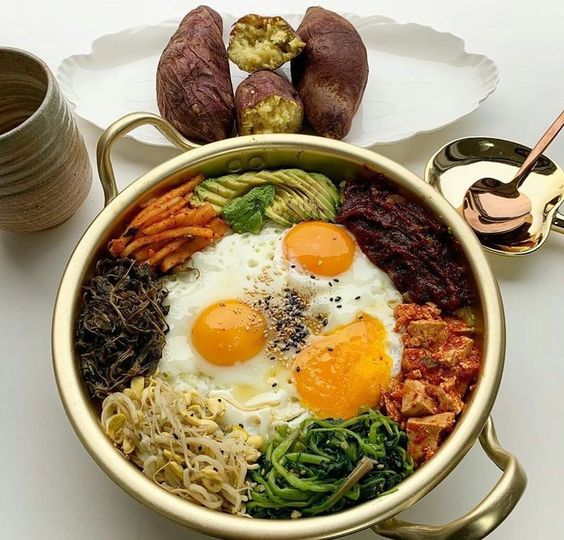 Korean bibimbap bowl with eggs, rice, vegetables, kimchi, sweet potatoes, and a cup of tea