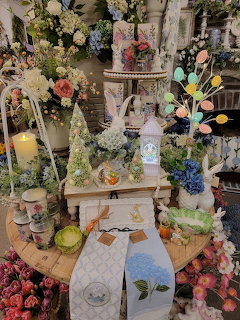 Easter boutique display with bunny figurines, colorful eggs, spring flowers, and decorative linens