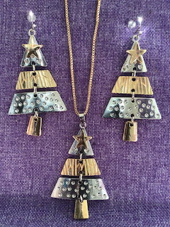 Christmas tree shaped necklace and earrings with decorative metal tiers displayed on purple textured fabric
