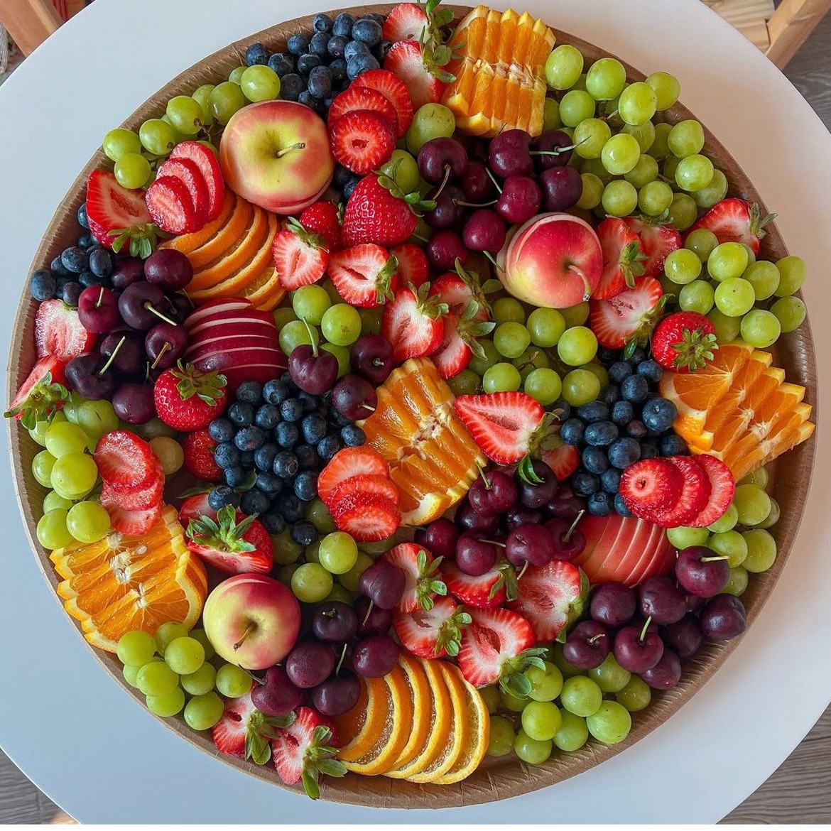 Overhead view of a circular white platter filled with assorted fresh fruits including berries, grapes, and sliced oranges