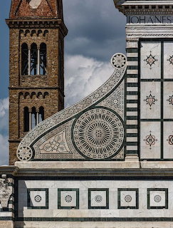 Ornate church facade with geometric stonework beside a brick bell tower under cloudy sky