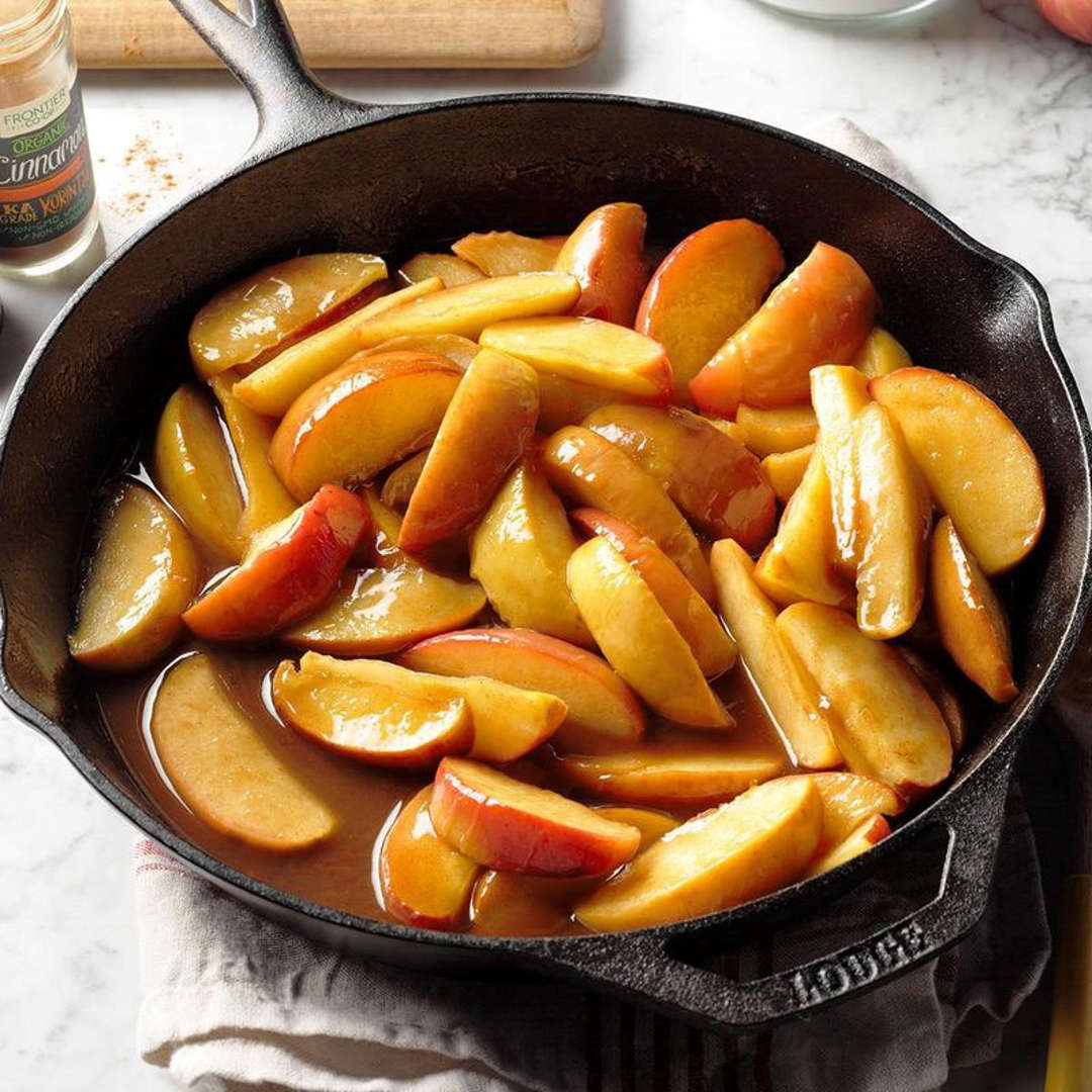 Golden caramelized apple slices in a black cast iron skillet on a marble counter