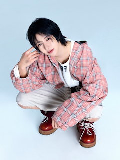 Person crouching in a studio wearing a pink plaid jacket, white pants, and brown shoes