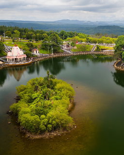 Small green island in a calm lake beside landscaped gardens and a pavilion
