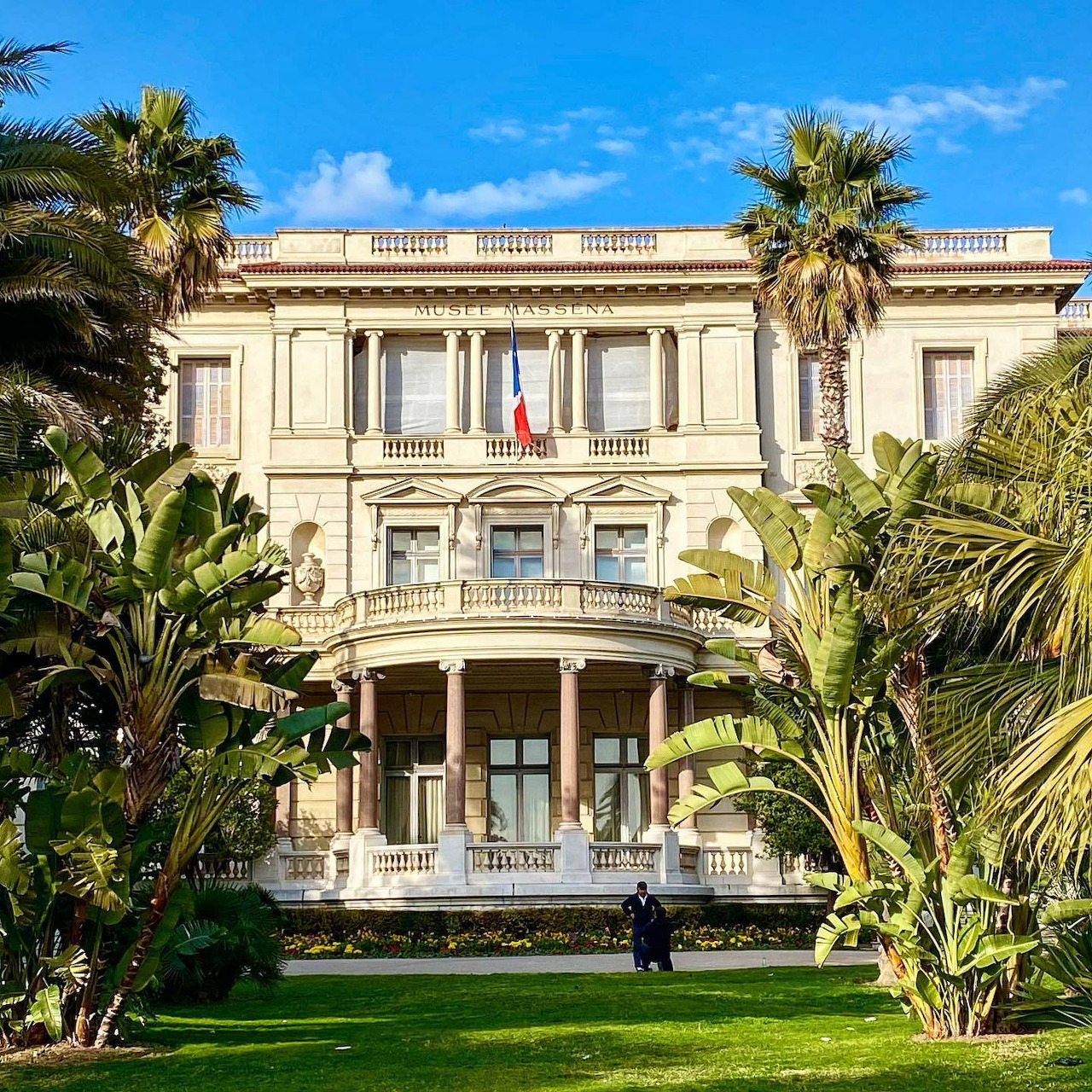 Neoclassical villa with columns and balustrades surrounded by palm trees and green gardens