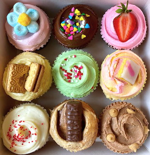 Top view of nine decorated cupcakes with colorful frosting, sprinkles, cookies, chocolate, and strawberry