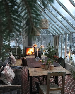 Festive greenhouse interior with fireplace, Christmas trees, candles, and rustic wooden table on brick floor