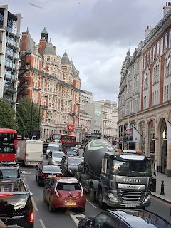 Traffic on a London street with historic buildings, buses, and a cement mixer