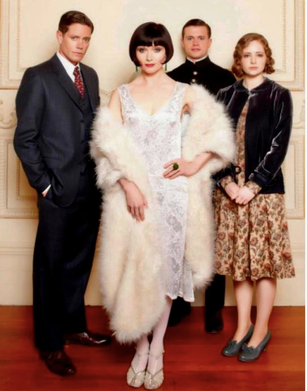 Four formally dressed people pose indoors in vintage-style clothing
