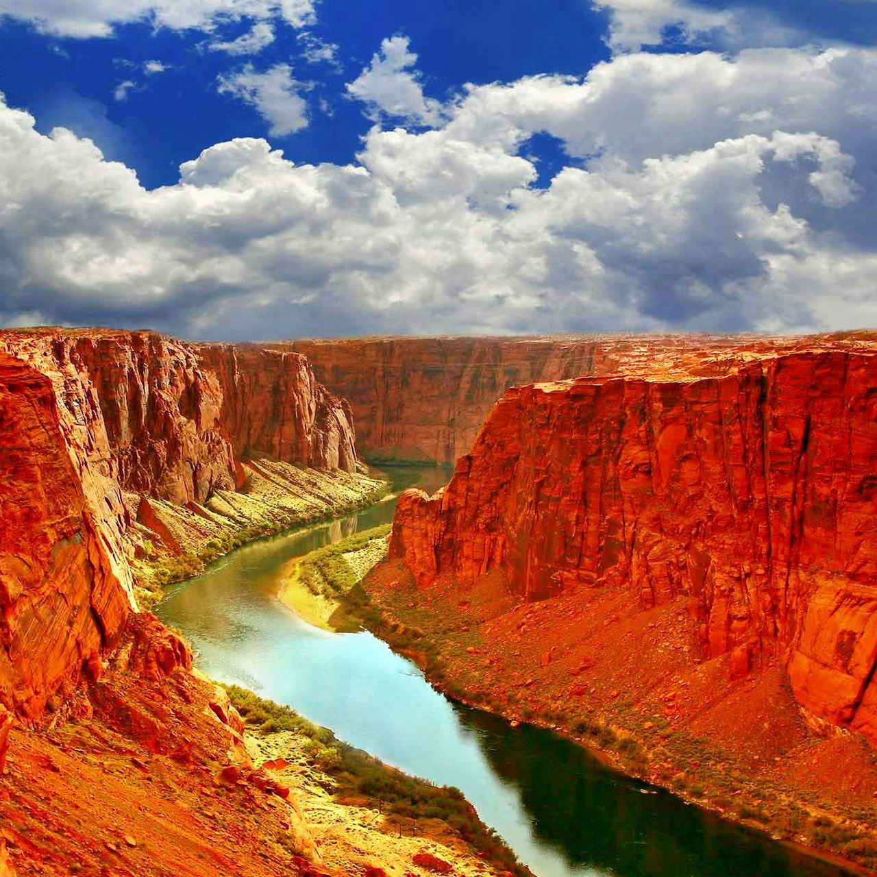 Aerial view of turquoise river flowing through red rock canyon with blue sky and clouds