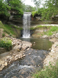 Minnehaha Falls waterfall flowing over a cliff surrounded by green summer trees in Minneapolis.