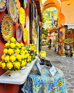 Market stall with lemons in bowl, decorative ceramic plates and pottery displayed along sunny Italian street