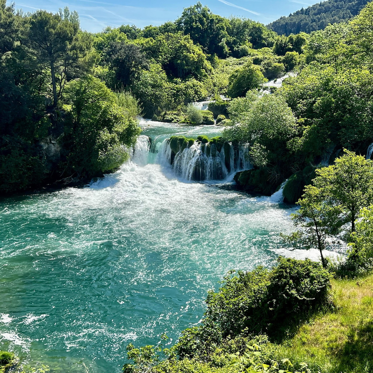 Small waterfall on a turquoise river surrounded by lush green forest