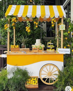 Yellow and white striped dessert cart with lemons, cakes, and green foliage background