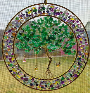Circular tree of life suncatcher hanging in a window with green leaves and purple beads