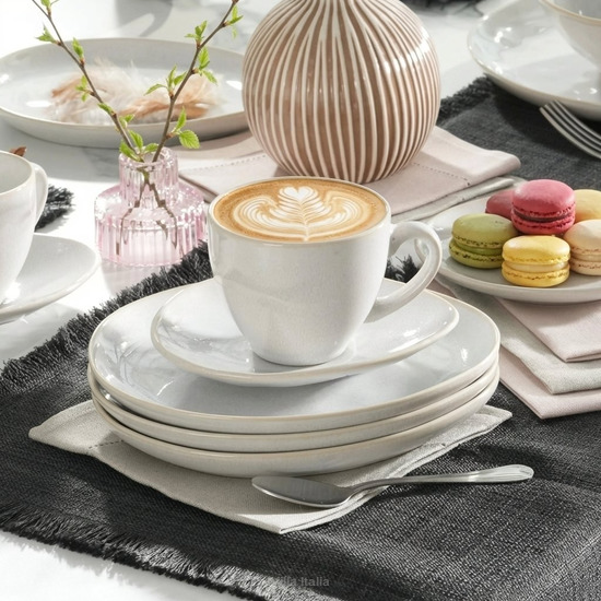 White cup of latte art coffee on stacked plates with colorful macarons on a table setting