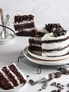 Chocolate layer cake with white cream frosting and cookie pieces, slice shown revealing interior layers