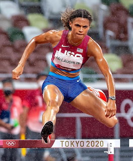Female athlete in mid-air during Olympic triple jump competition wearing red and blue uniform