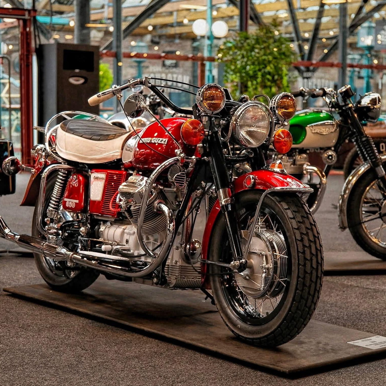 Red vintage Guzzi motorcycle on showroom floor with other classic bikes behind