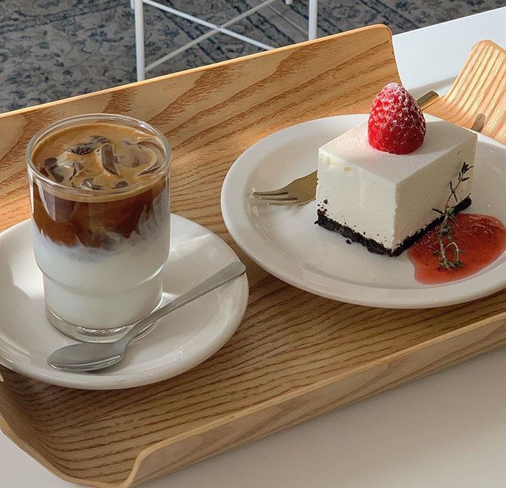 Iced coffee and strawberry cheesecake on white plates on a wooden tray