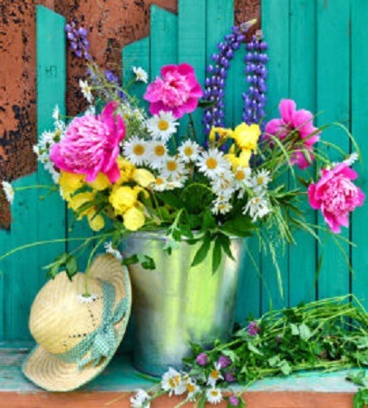 Colorful flower arrangement in green bucket with straw hat and turquoise fence background
