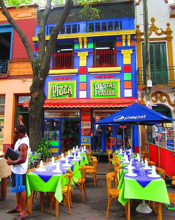 Brightly painted colorful cafe exterior with outdoor dining tables and chairs on sidewalk