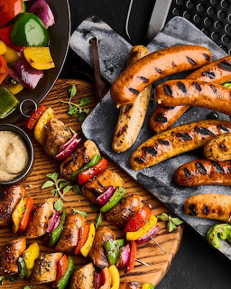 Grilled sausages and kebabs with pepers on wooden cutting board, overhead food photography