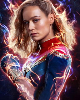 Captain Marvel in red and blue suit with glowing energy effects against cosmic background
