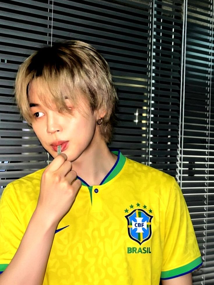 Young man with blonde hair in yellow Brazil soccer jersey posing with hand near face
