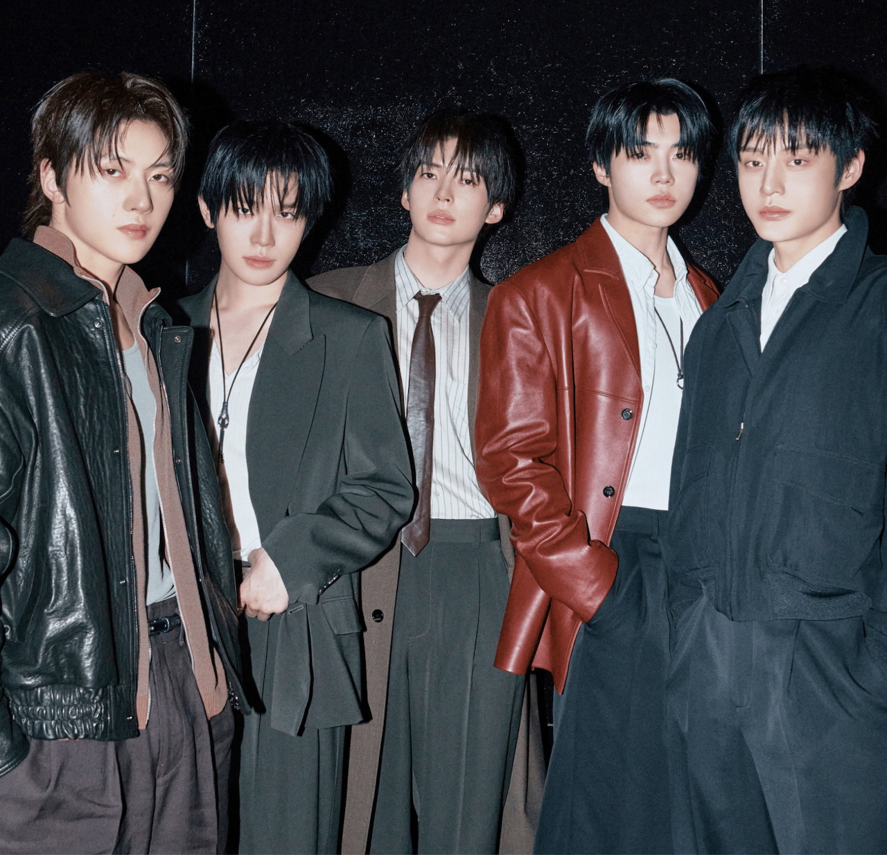 Five young men in fashionable jackets standing together against dark backdrop