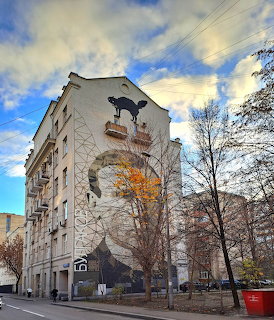Large portrait mural painted on apartment building facade with autumn trees and cloudy sky
