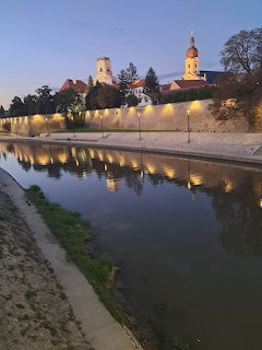 Riverside view of Győr Hungary at dusk with illuminated walls and church tower reflected in water
