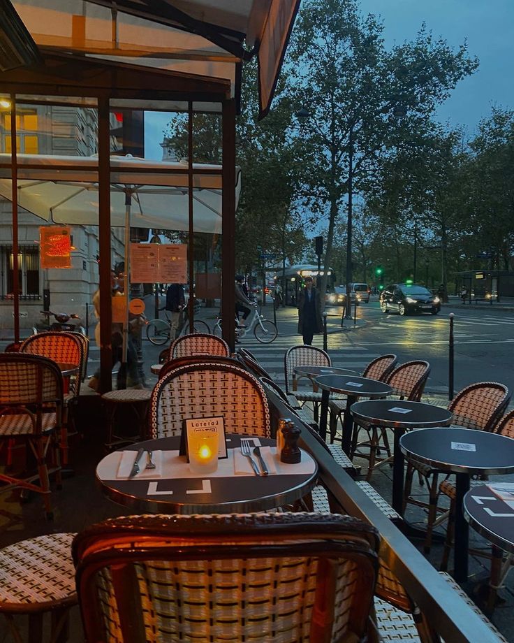 Café terrace at dusk with wicker chairs, candles, and street view through windows