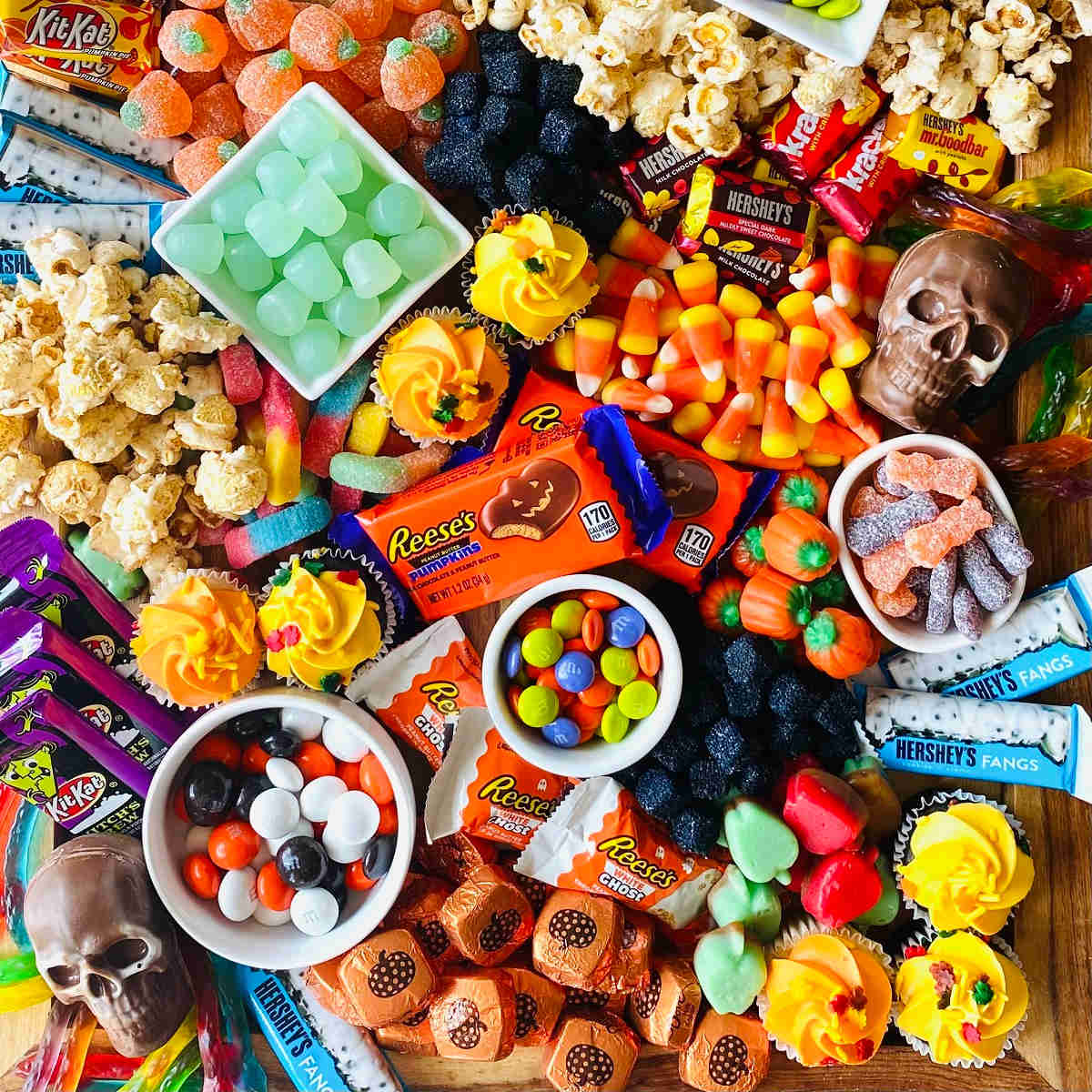 Overhead view of Halloween candy assortment with chocolates, popcorn, candy corn, and pumpkin decorations on wood table
