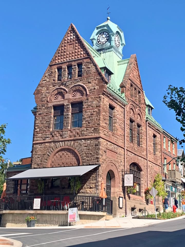 Historic stone post office building with clock tower and green copper roof under blue sky
