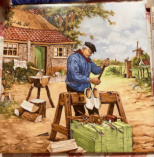 Painting of a Dutch clog maker carving wooden clogs outside a cottage with a windmill behind