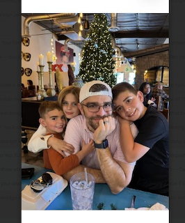 Father with three kids posing at a restaurant table with a Christmas tree behind them