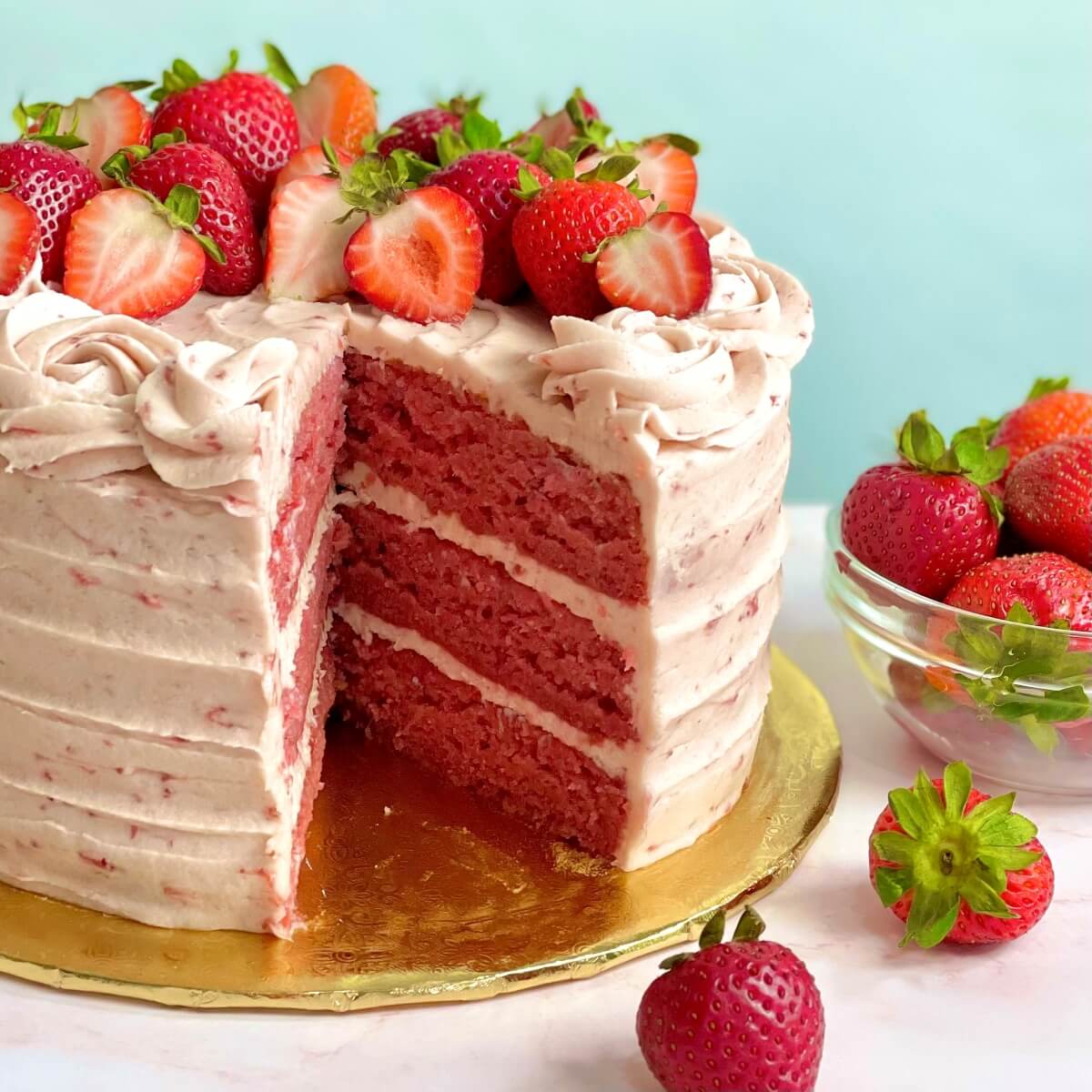 Pink frosted layer cake with fresh strawberries on top, slice removed showing pink layers