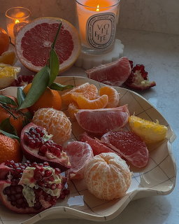 Plate with mandarins, grapefruit slices, pomegranate halves, and lit candles on a windowsill