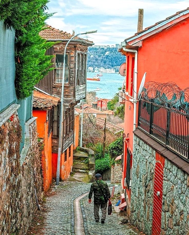 Person walking down colorful Mediterranean alley with orange buildings leading to sea view