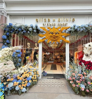 Boutique entrance decorated with flowers, a large sun ornament, and teddy bears